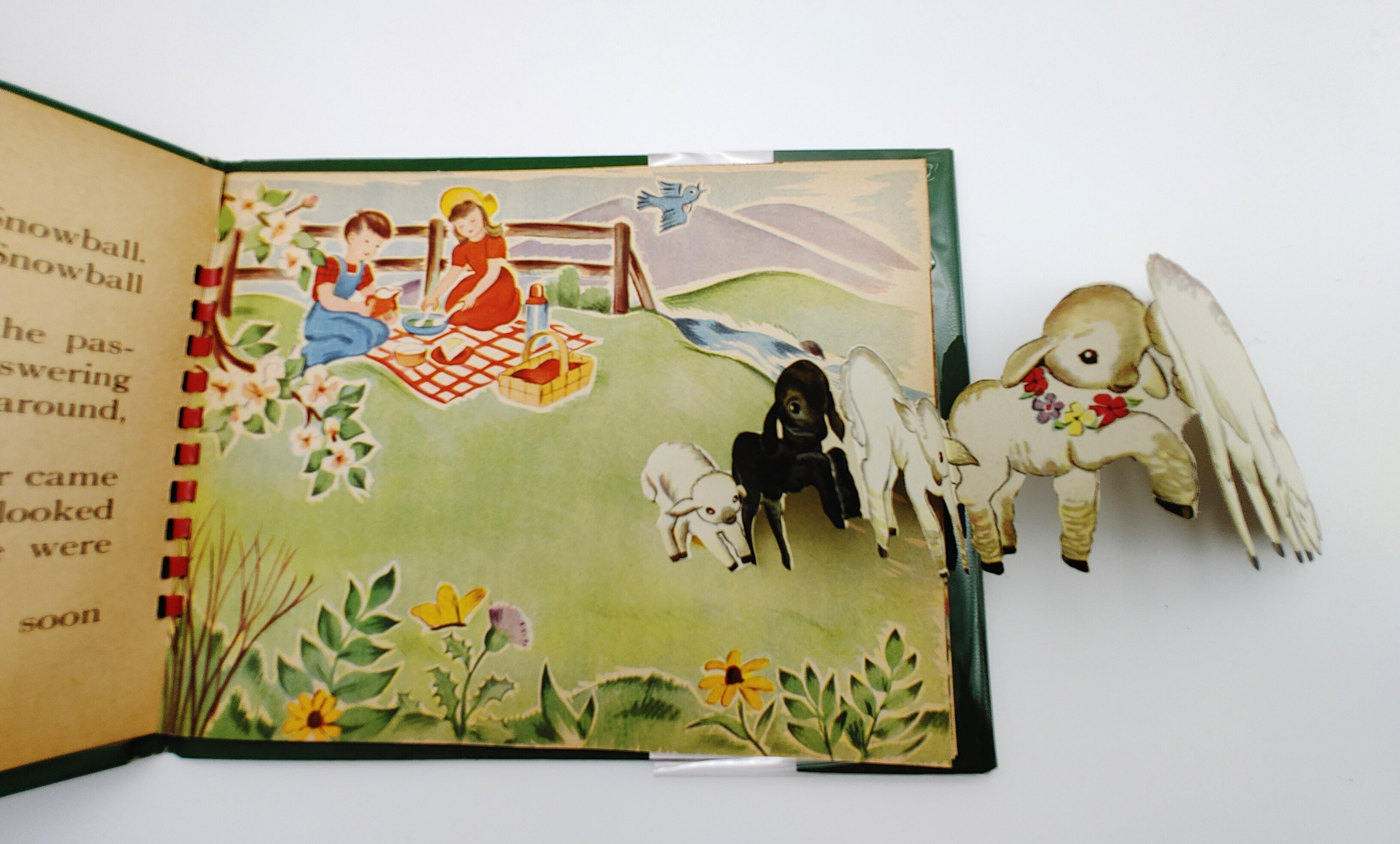 Pop-up book illustration of a series of sheep in a field where children are picnicking